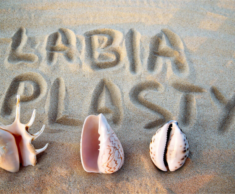 The word labiaplasty is drawn in sand with three seashells underneath.