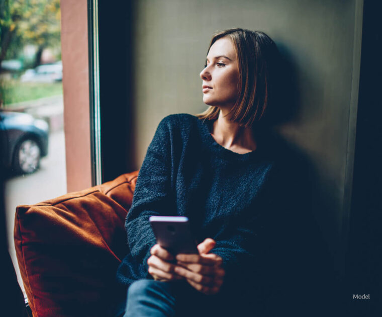 woman sits in a chair, looking away from the camera with a pensive look on her face