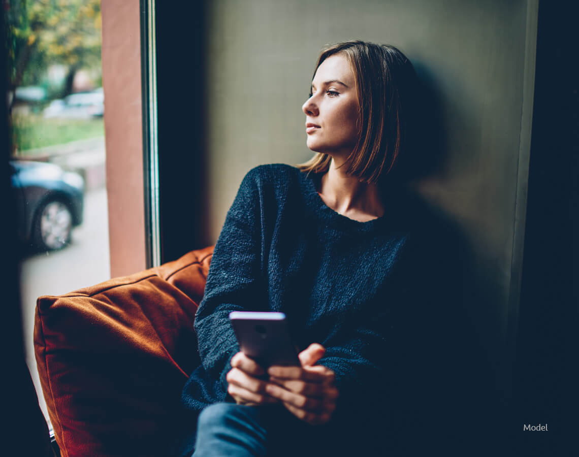 woman sits in a chair, looking away from the camera with a pensive look on her face