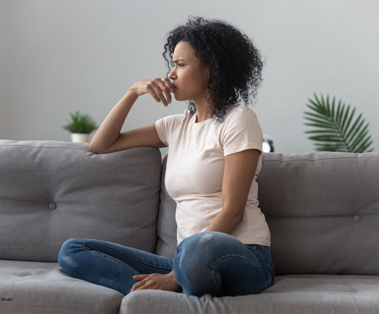 Sad thoughtful worried African American girl sitting on the sofa looking away